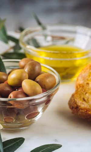 A closeup shot of slices of bread with extra virgin oil near glass bowls filled with oil and olives